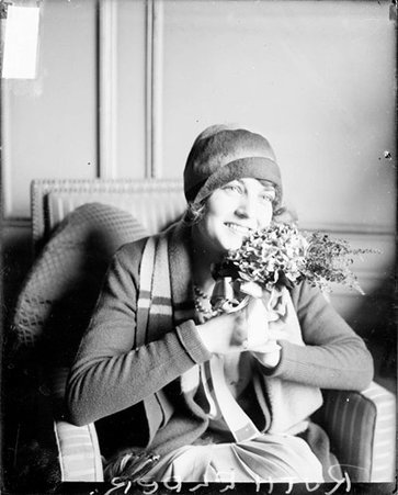 Pilot Ruth Elder holding a floral arrangement, sitting in a room - Chicago Daily News, Inc.