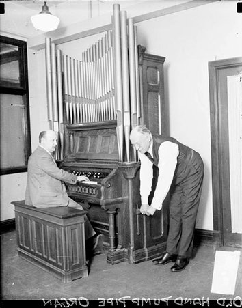 Two unidentified men playing a hand pump pipe organ in a room - Chicago Daily News, Inc.