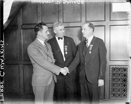 Alvin Carter and Ferre Watkins standing and shaking hands in a room, Howard Savage standing between them, dark exposure - Chicago Daily News, Inc.