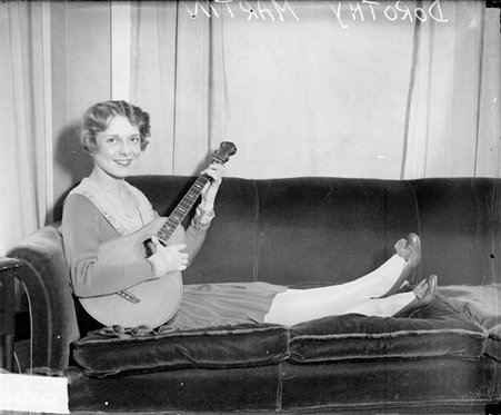 Dorothy Martin playing a mandolin and looking toward the camera, reclining on a sofa - Chicago Daily News, Inc.