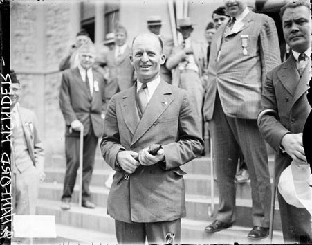 Hanaford McNider standing on the steps in front of a building, men standing in the background - Chicago Daily News, Inc.