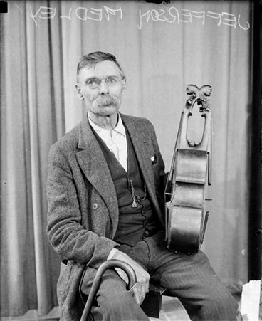 Jefferson Medley holding a sting instrument, sitting in front of a backdrop in a room - Chicago Daily News, Inc.