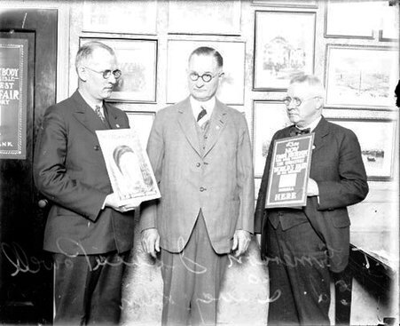 Isaac N. Powell standing with two men in a room, holding promotional materials for the 1933 World's Fair - Chicago Daily News, Inc.