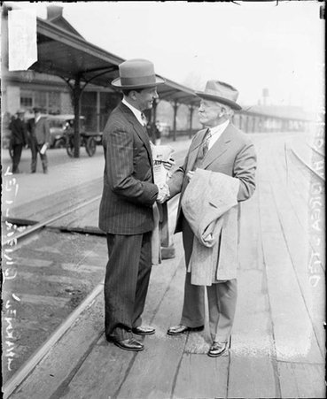 Dr. James F. Breasted shaking hands, standing outside on a train platform at a railroad station - Chicago Daily News, Inc.