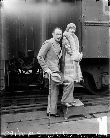 Mr. and Mrs. Rod La Rocque standing in front of passenger train car in a train station, dark exposure - Chicago Daily News, Inc.