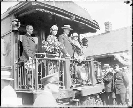 President and Mrs. Calvin Coolidge standing with an unidentified woman on the rear platform of a train car at a railroad depot, viewed at an angle - Chicago Daily News, Inc.