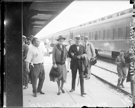 Mrs. Charles Gibson and Mr. John Davis walking on an outdoor train platform in a railroad station - Chicago Daily News, Inc.