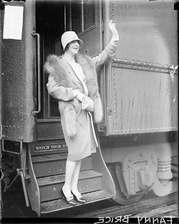 Fanny Brice standing and waving on the steps of a passenger train car in a railroad station - Chicago Daily News, Inc.