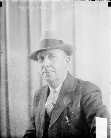 John F. Emery looking toward the camera, sitting in front of a backdrop in a room - Chicago Daily News, Inc.
