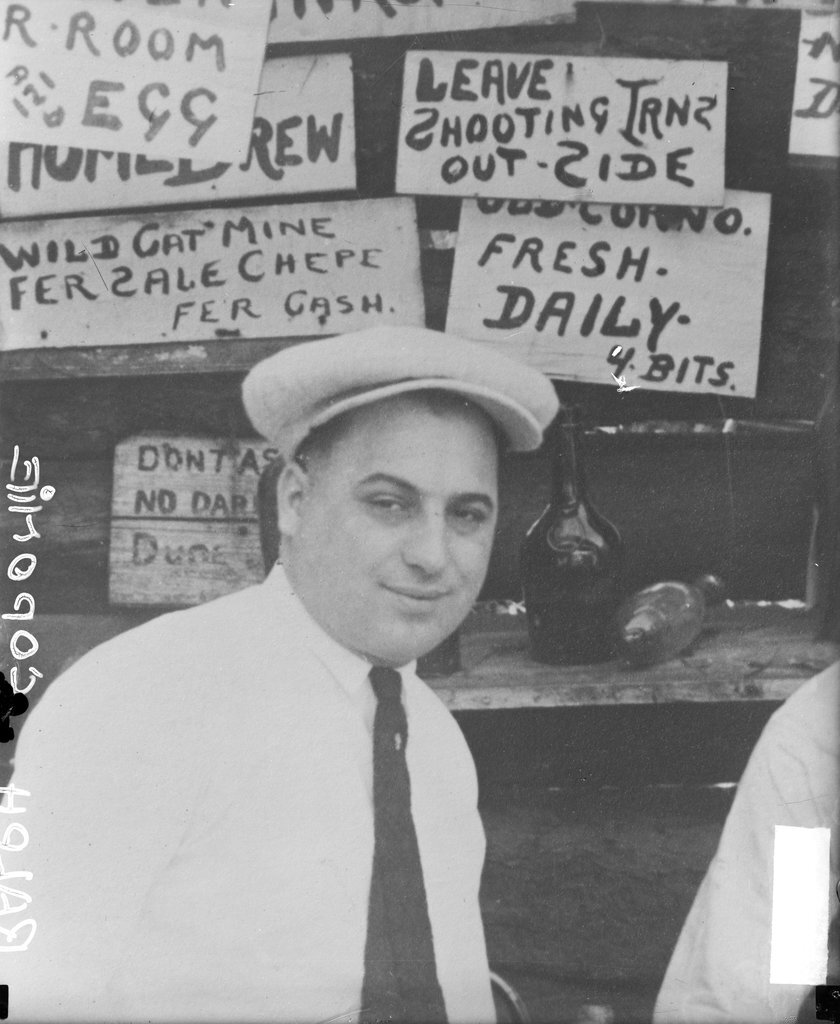 Ralph Capone looking toward the camera, standing in front of a food stand - Chicago Daily News, Inc.