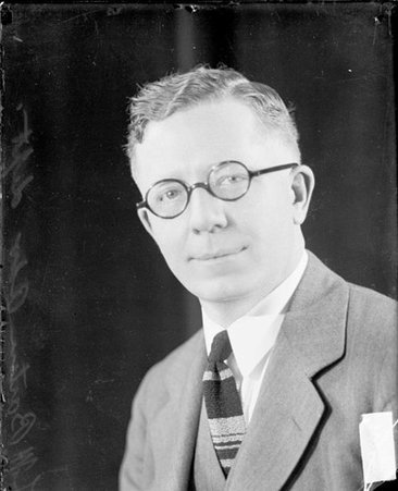 L. M. Barton looking toward the camera, sitting in a room, dark exposure - Chicago Daily News, Inc.