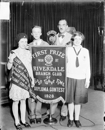 Russell Pratt standing with winners of the Topsy Turvy Time diploma contest in front of a dark backdrop in a room - Chicago Daily News, Inc.