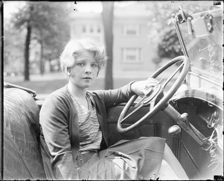 Mary E. Fahreny looking toward the camera, sitting in the driver's seat of a convertible automobile, light exposure - Chicago Daily News, Inc.