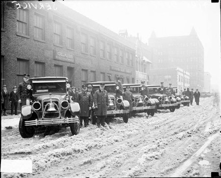 Fire department trucks lined up on snowy street, warehouse in background - Chicago Daily News, Inc.
