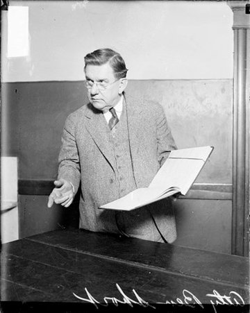 Attorney Benedict Short pointing and holding an open book - Chicago Daily News, Inc.