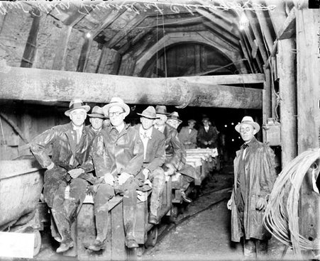 Men sitting and riding on a railroad cart in an underground tunnel during the construction of the Chicago Avenue water tunnel - Chicago Daily News, Inc.