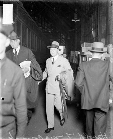 Harold F. McCormick looking toward the camera, walking next to a passenger train car in a railroad station - Chicago Daily News, Inc.