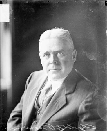 Clyde T. Brown, Chicago Daily News photographer, looking toward the camera, sitting in front of a dark backdrop in a room, light exposure - Chicago Daily News, Inc.
