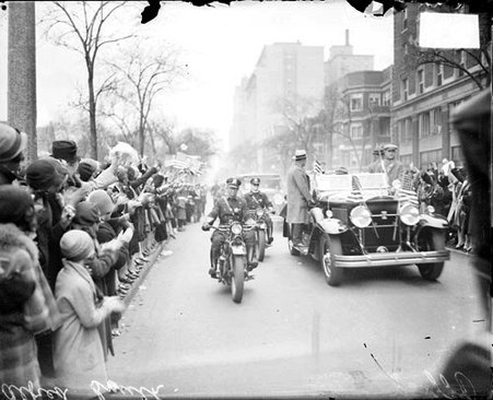 Alfred E. Smith parade, two police officers accompanying a convertible with men, standing on the rails of the automobile, past crowds are lining the street - Chicago Daily News, Inc.