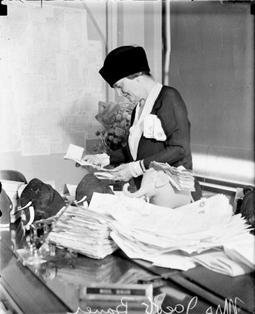 Mrs. Bertha Bauer, standing at a desk covered with papers in a room - Chicago Daily News, Inc.