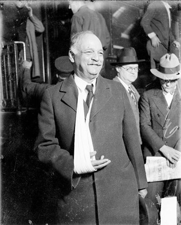 Charles Curtis, U. S. looking to this left, standing in front of a passenger train car in a railroad station, men wearing suits and railroad employees standing in the background - Chicago Daily News, Inc.