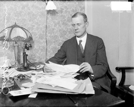 John A. Swanson, Cook County State's Attorney and Cook County Circuit Court judge, sitting at desk, reading a piece of paper in his hand, light exposure - Chicago Daily News, Inc.