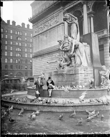 Woman and man feeding pigeons, standing in front of the Fountain of the Great Lakes - Chicago Daily News, Inc.