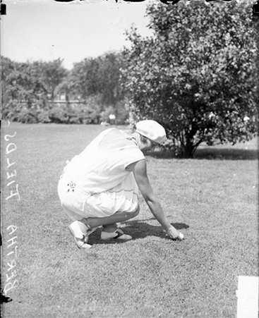 Bertha Fields setting a golf ball on a tee and kneeling on a lawn - Chicago Daily News, Inc.