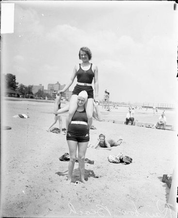 Woman wearing a bathing suit and sitting on the shoulders of another woman wearing a bathing suit and standing on the sand at Rogers Park bathing beach in Chicago - Chicago Daily News, Inc.