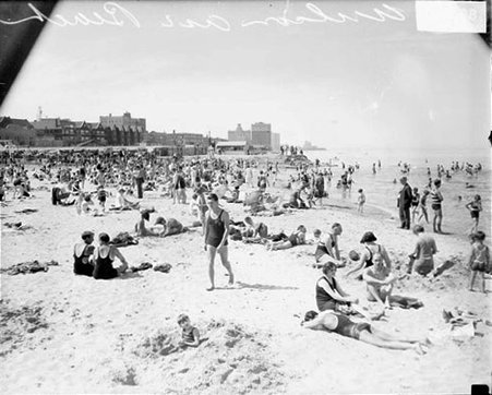 Crowds of people wearing bathing suits or street clothes and sitting, lying, and standing on the sand or swimming and standing in the water at Wilson Avenue bathing beach - Chicago Daily News, Inc.