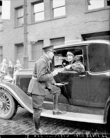 Linnea Carlson and Thomas Weenhoff, police officer, who is sitting in the driver's seat of the automobile and looking down at the piece of paper - Chicago Daily News, Inc.