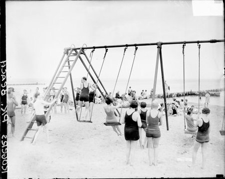 Children and adults wearing bathing suits and sitting and standing on swings at Rogers Park bathing beach, - Chicago Daily News, Inc.