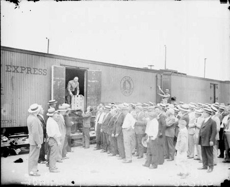 Chicago produce terminal, where a man on a train is handing a large box to a man on the ground - Chicago Daily News, Inc.