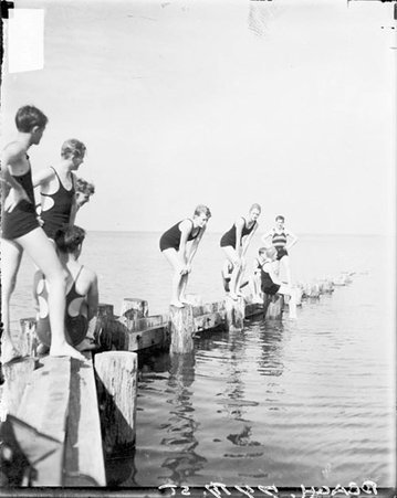 Two young women wearing bathing suits standing on a narrow wooden jetty in Lake Michigan at the 74th Street beach - Chicago Daily News, Inc.