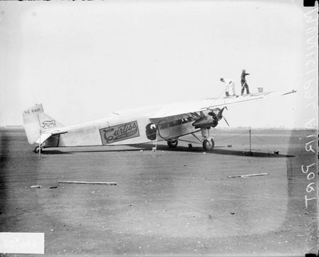 Men holding mops and cleaning the wing of a Curtiss airplane, standing on the wing of the airplane on an airfield at Municipal Airport - Chicago Daily News, Inc.