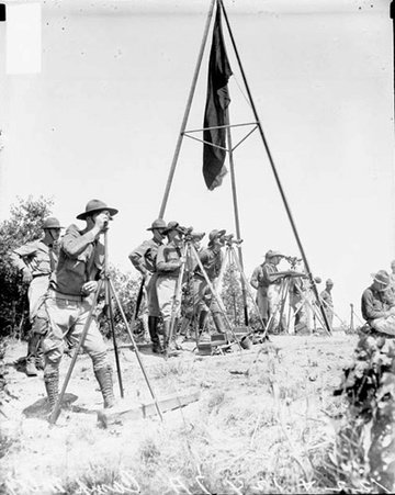 Soldiers from the 122nd and 124th Field Artillery Regiments standing behind viewing instruments mounted on tripods next to a pole frame on a field at Camp McCoy - Chicago Daily News, Inc.