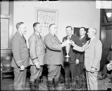 Major John Bauder, detective John O'Malley, Ben Hazare, Leo Black, Sergeant Sam Peterson, and Capt. James Mooney holding a large trophy - Chicago Daily News, Inc.