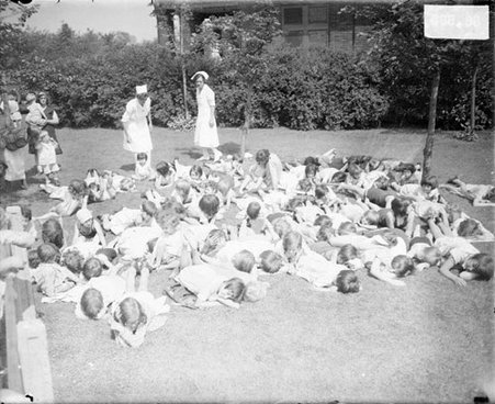 Group of girls lying on a lawn in front of a building at the Chicago Daily News Sanitarium - Chicago Daily News, Inc.