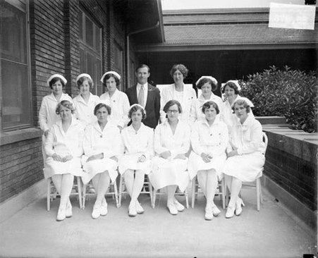 Eleven nurses, Dr. Marion Crane, Superintendent of the Chicago Daily News Sanitarium, and an unidentified man posing on a walkway in front of a building at the Chicago Daily News Sanitarium, light exposure - Chicago Daily News, Inc.