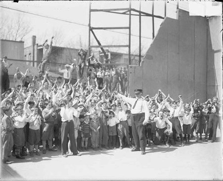Crowd of boys standing and cheering on a street in front of a metal tower and wires - Chicago Daily News, Inc.
