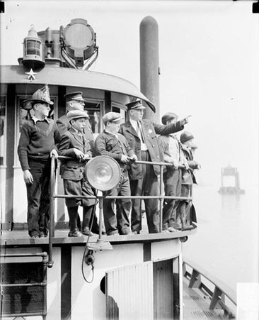 Two firefighters standing with a group of boys on the deck of a ship sitting in a body of water - Chicago Daily News, Inc.