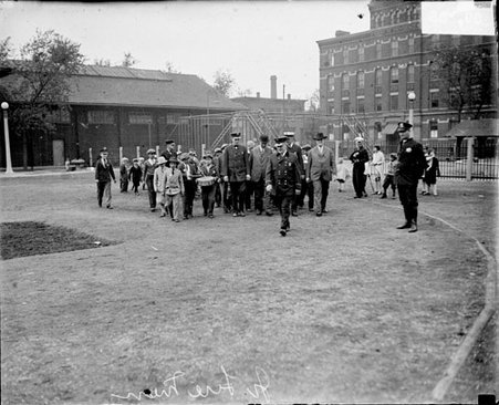 Group of firefighters and boys walking on a field in front of a building - Chicago Daily News, Inc.