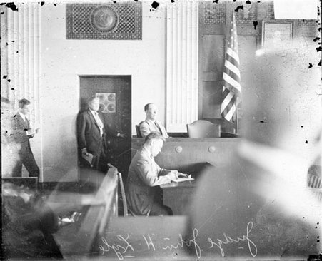 Cook County Municipal Court Judge John H. Lyle sitting behind a podium in a courtroom - Chicago Daily News, Inc.