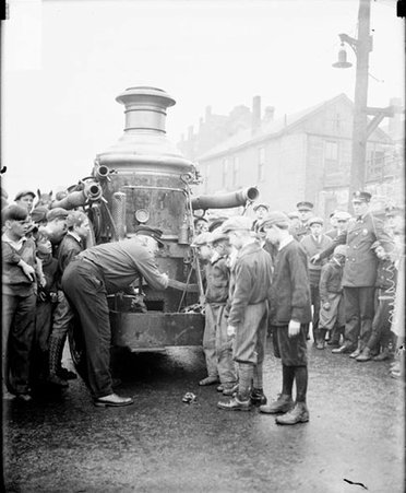 Firefighters and a group of boys standing in front of a horse-drawn water wagon on a street - Chicago Daily News, Inc.