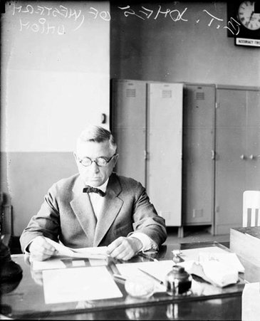 B. T. Jones looking at a piece of paper, sitting at a desk in a room - Chicago Daily News, Inc.