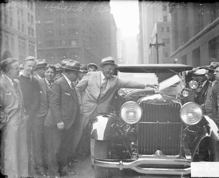 William E. Russell standing next to a new police automobile on a street, lifting the automobile's hood, light exposure - Chicago Daily News, Inc.