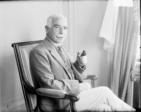 Otto Kahn looking toward the camera, holding up a pipe in his hand, sitting in a room - Chicago Daily News, Inc.