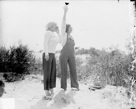 Two women standing on the sand at a beach at Indiana Dunes, one waving and the other calling out - Chicago Daily News, Inc.