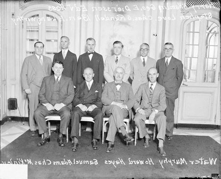 Ten men sitting and standing in a room - Chicago Daily News, Inc.