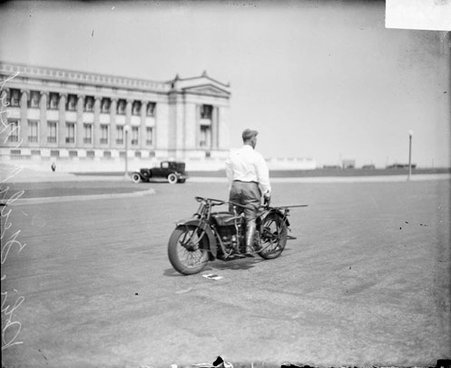 Police officer standing backwards on a motorcycle on a street in front of the Field Museum of Natural History - Chicago Daily News, Inc.